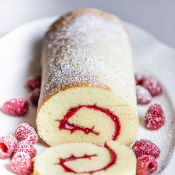 swiss roll cake with raspberries on white plate