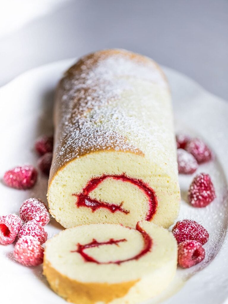 swiss roll cake with raspberries on white plate