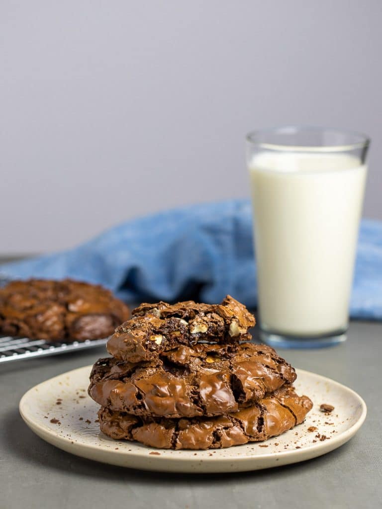 chocolate cookies stacked on plate in front of glass of milk and blue napkin