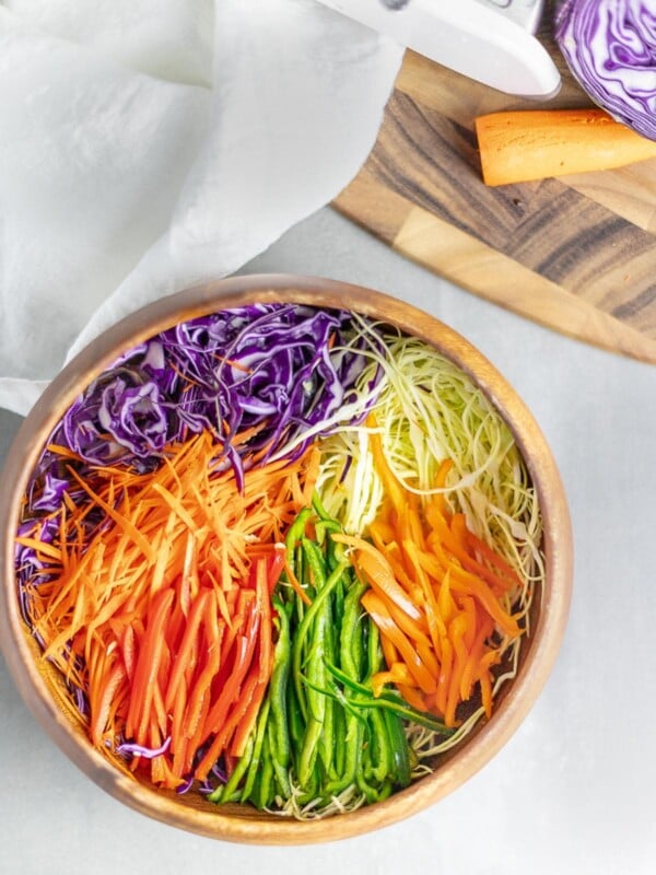rainbow cabbage salad in wooden bowl next to cutting board