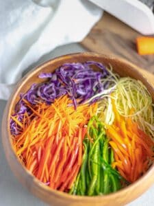 rainbow cabbage salad in wooden bowl next to cutting board