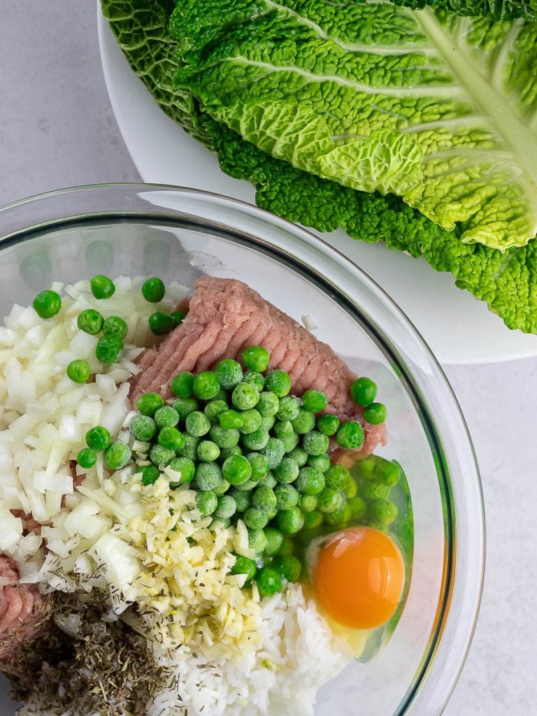 cabbage roll ingredients in a bowl with egg, peas, and cabbage leaves