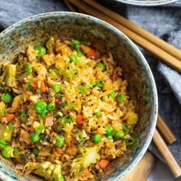 ketchup fried rice with peas and vegetables in two bowls with chopsticks