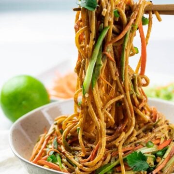 Thai peanut noodles in a bowl held by chopsticks