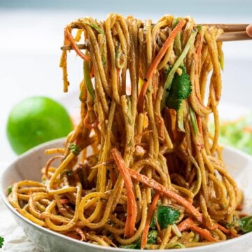 Thai peanut noodles in a bowl held by chopsticks
