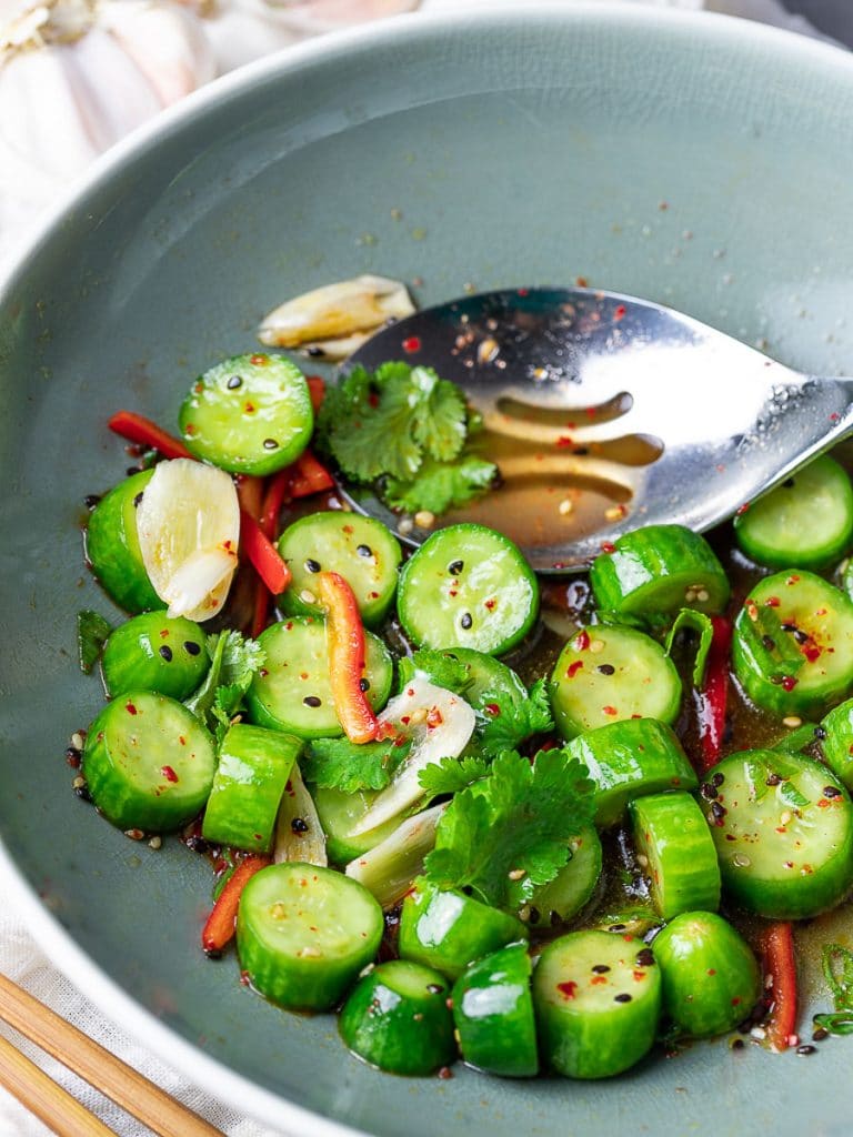Spicy Asian cucumber salad with herbs and red pepper in a blue bowl with a spoon