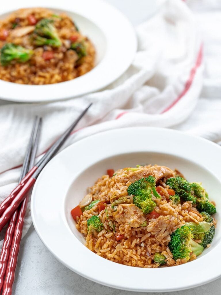 Thai red curry chicken fried rice with broccoli and chicken in white bowls with chopsticks