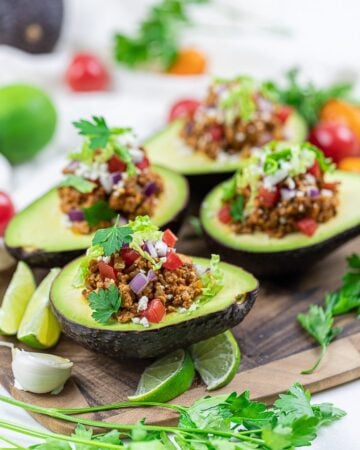 Keto taco stuffed avocado boats with lime, taco meat, tomatoes, and cilantro on a wooden board