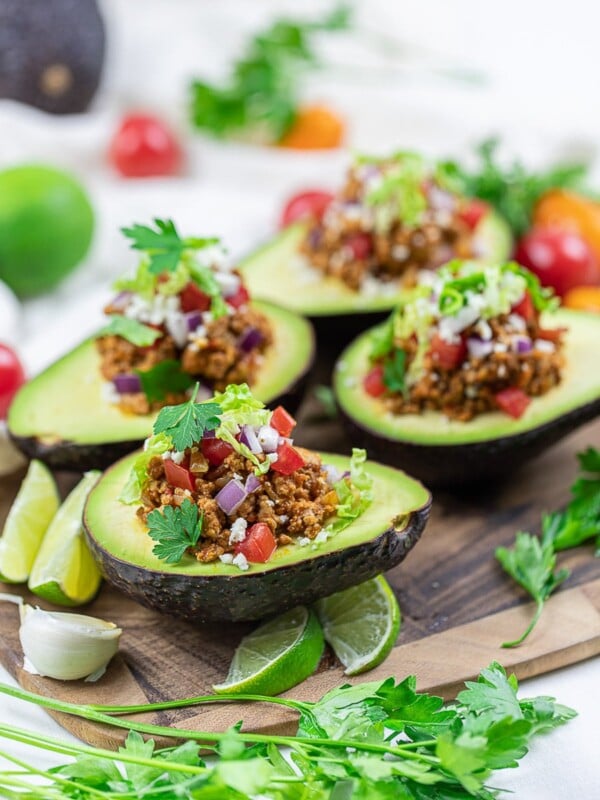 Keto taco stuffed avocado boats with lime, taco meat, tomatoes, and cilantro on a wooden board