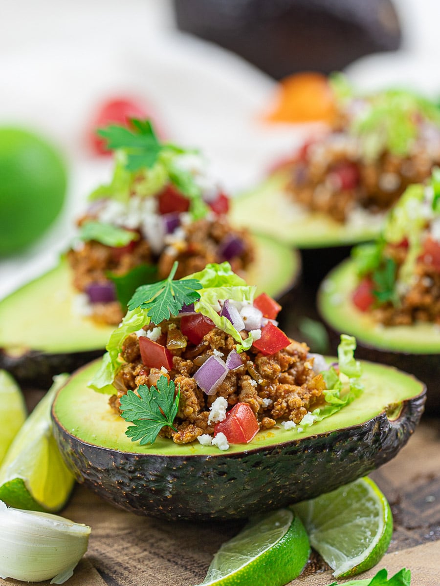 Keto taco avocado boats with lime, taco meat, tomatoes, and cilantro on a white plate.