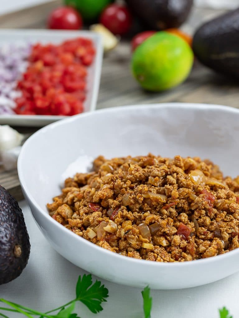 taco meat filling in a white bowl with tomatoes, lime, and avocado