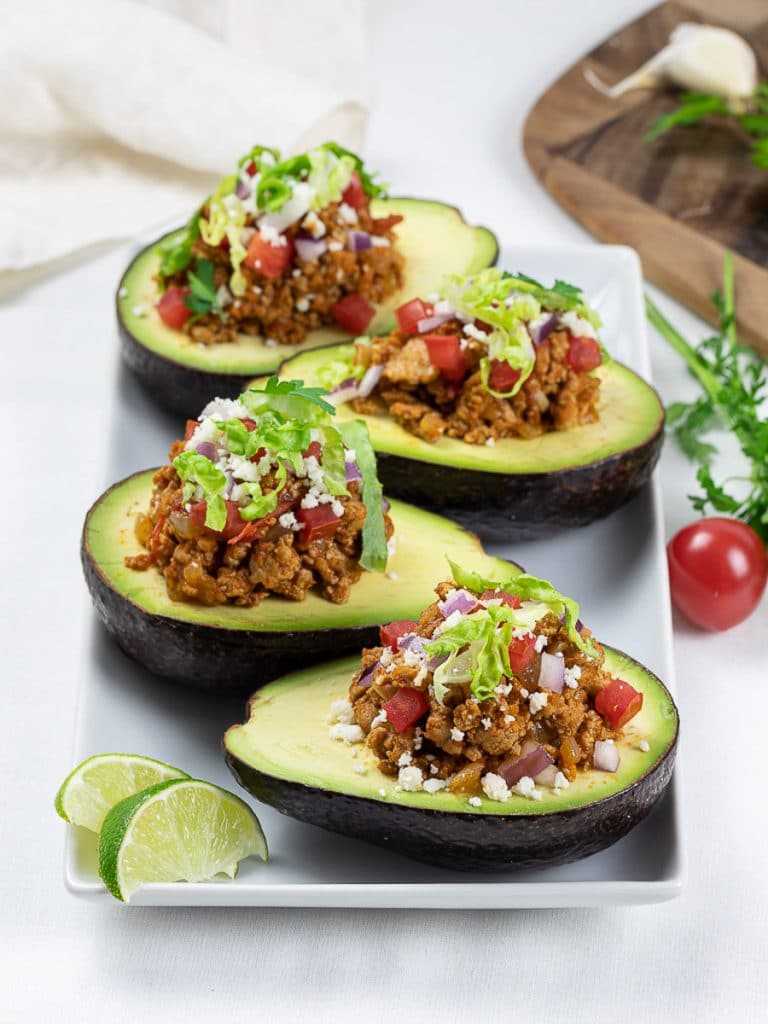Keto taco stuffed avocado boats with lime, taco meat, tomatoes, and cilantro on a white plate