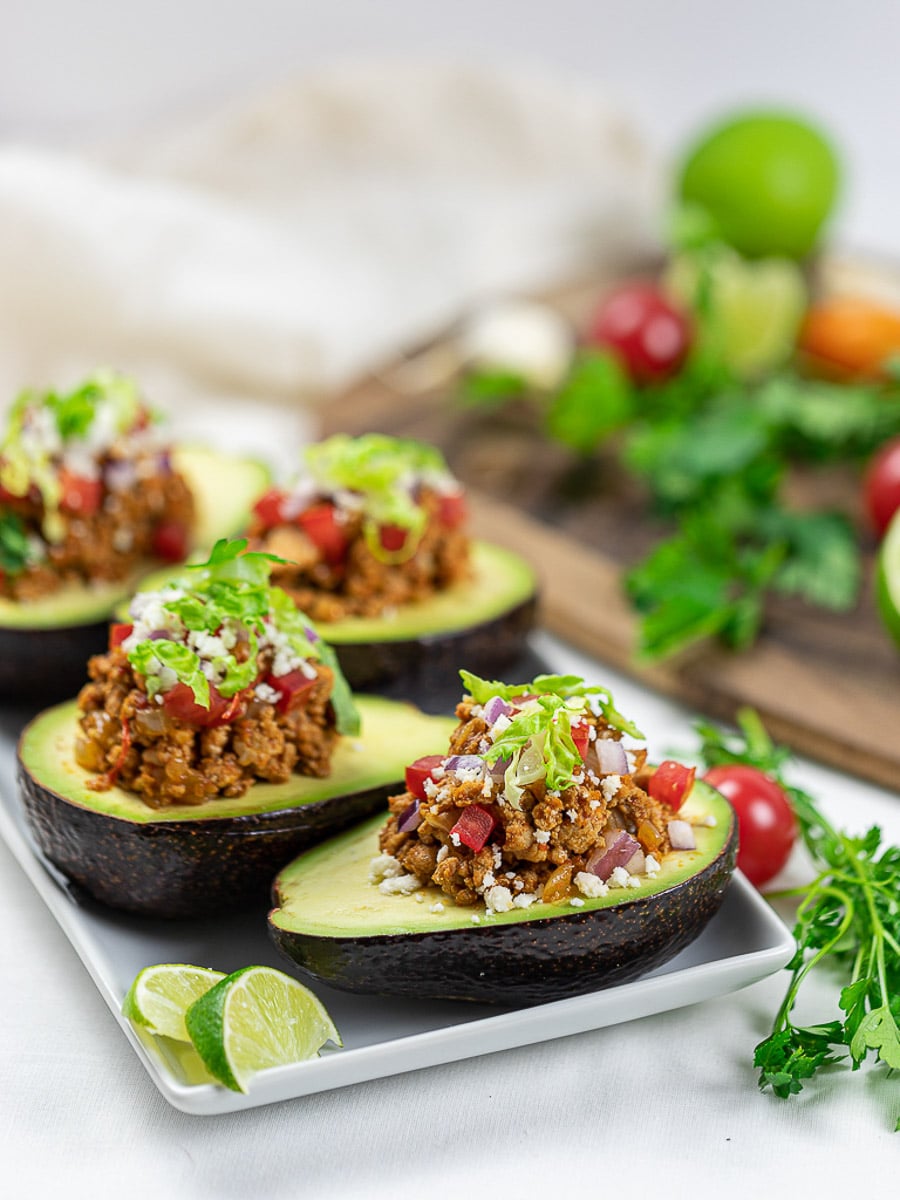 Taco stuffed avocado boats with lime, taco meat, tomatoes, and cilantro on a white plate.