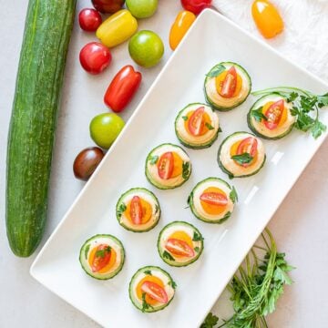 vegan cucumber hummus bites with red and orange cherry tomatoes on a white plate