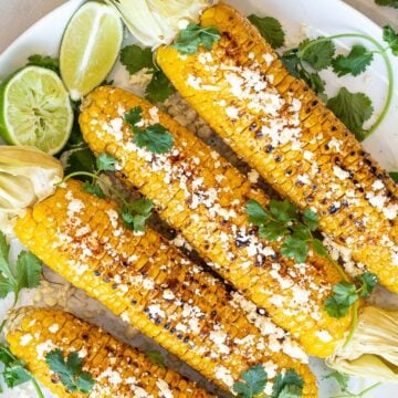 Healthy Grilled Mexican Street Corn on the cob (Elotes) with lime, cilantro, and cotija cheese on a white plate
