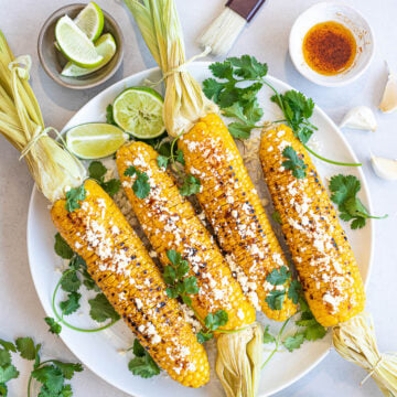 Healthy Grilled Mexican Street Corn (Elotes) with lime, cotija cheese, and cilantro on a white plate