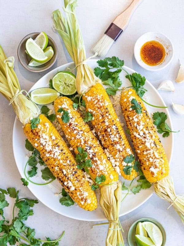 Healthy Grilled Mexican Street Corn (Elotes) with lime, cotija cheese, and cilantro on a white plate