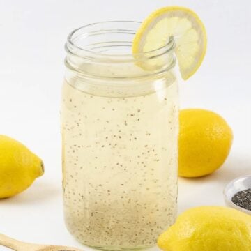 Chia fresca, chia lemonade in a mason jar next to lemons and chia seeds on a white surface