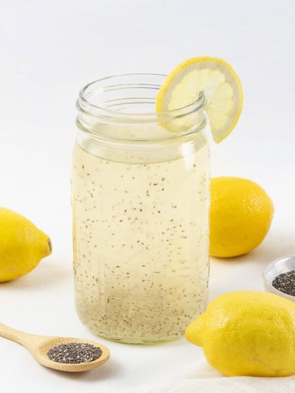 Chia fresca, chia lemonade in a mason jar next to lemons and chia seeds on a white surface