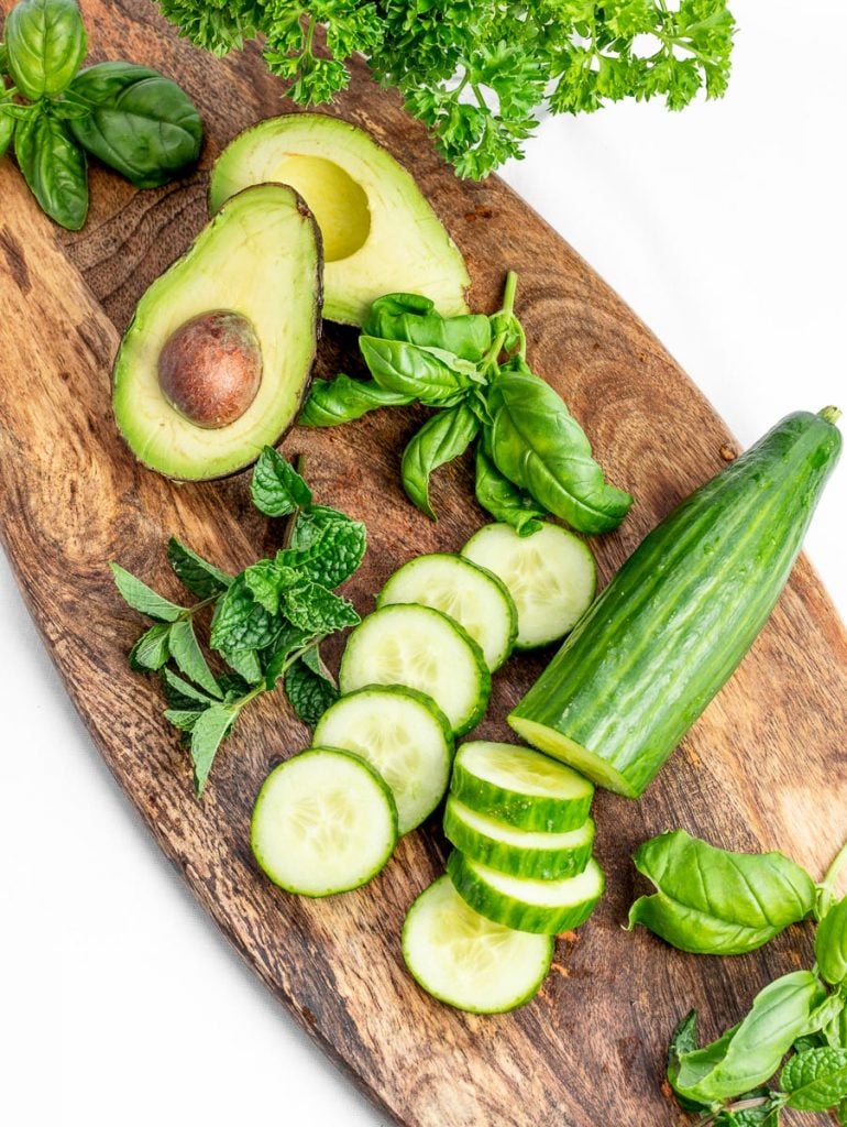 cucumber, avocado, mint, basil, and parsley on a wooden board