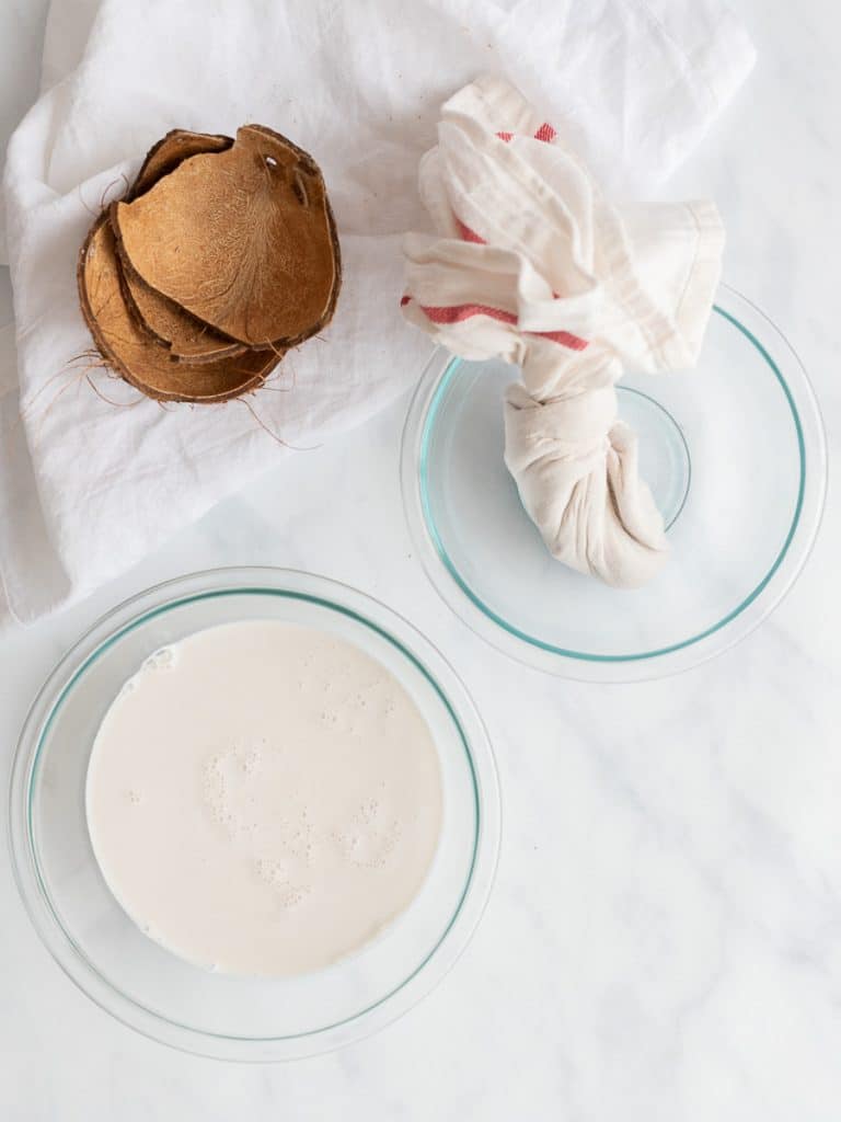 homemade coconut milk in a bowl with cheesecloth and coconut shells