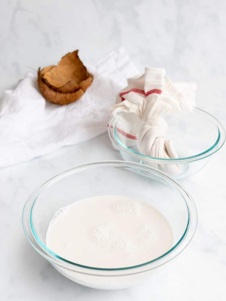 homemade coconut milk in a bowl with cheesecloth and coconut shells