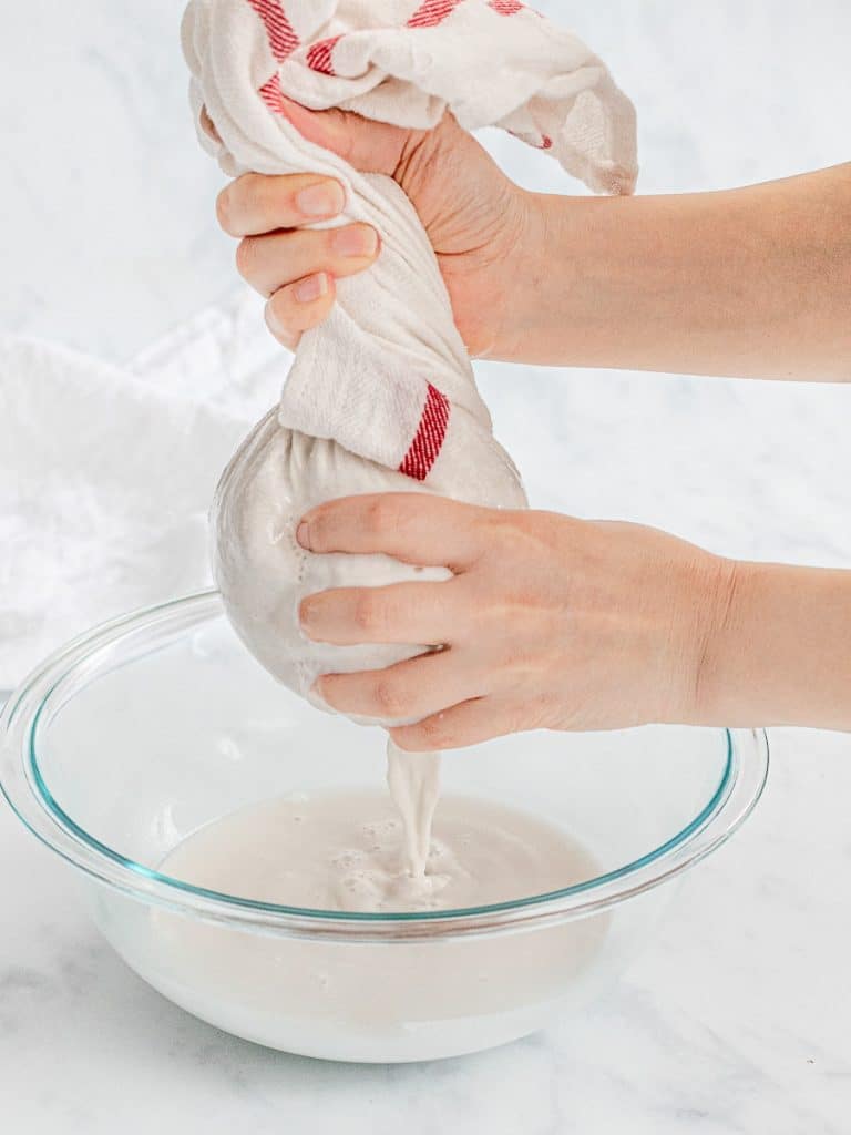 squeezing out homemade coconut milk in a cheesecloth into a glass bowl