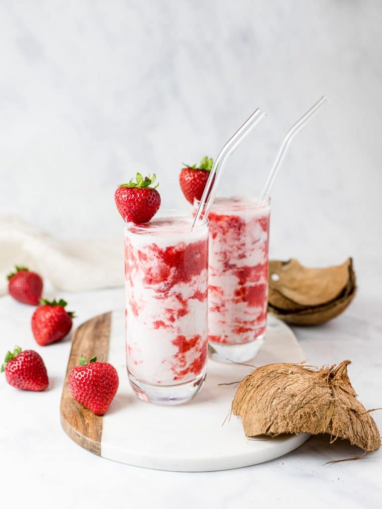 homemade Korean strawberry milk in two glasses with straws surrounded by strawberries