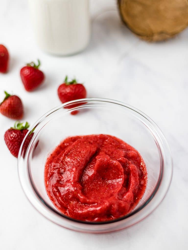 strawberry puree in a glass bowl surrounded by strawberries