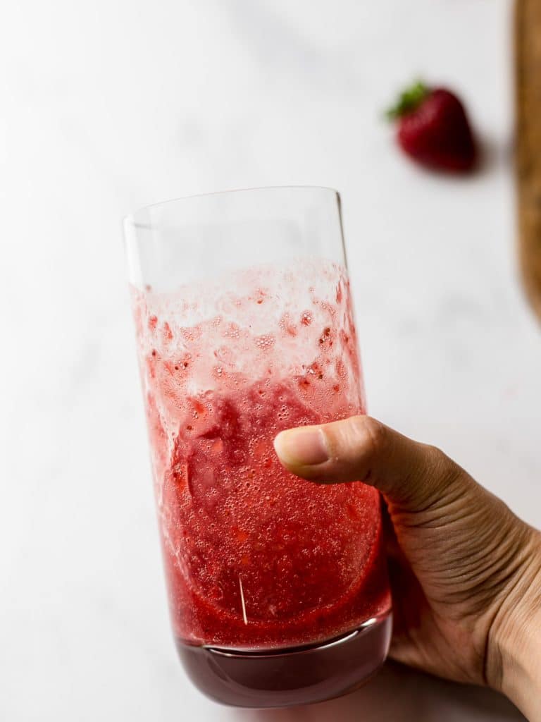 strawberry puree in a glass held in hand
