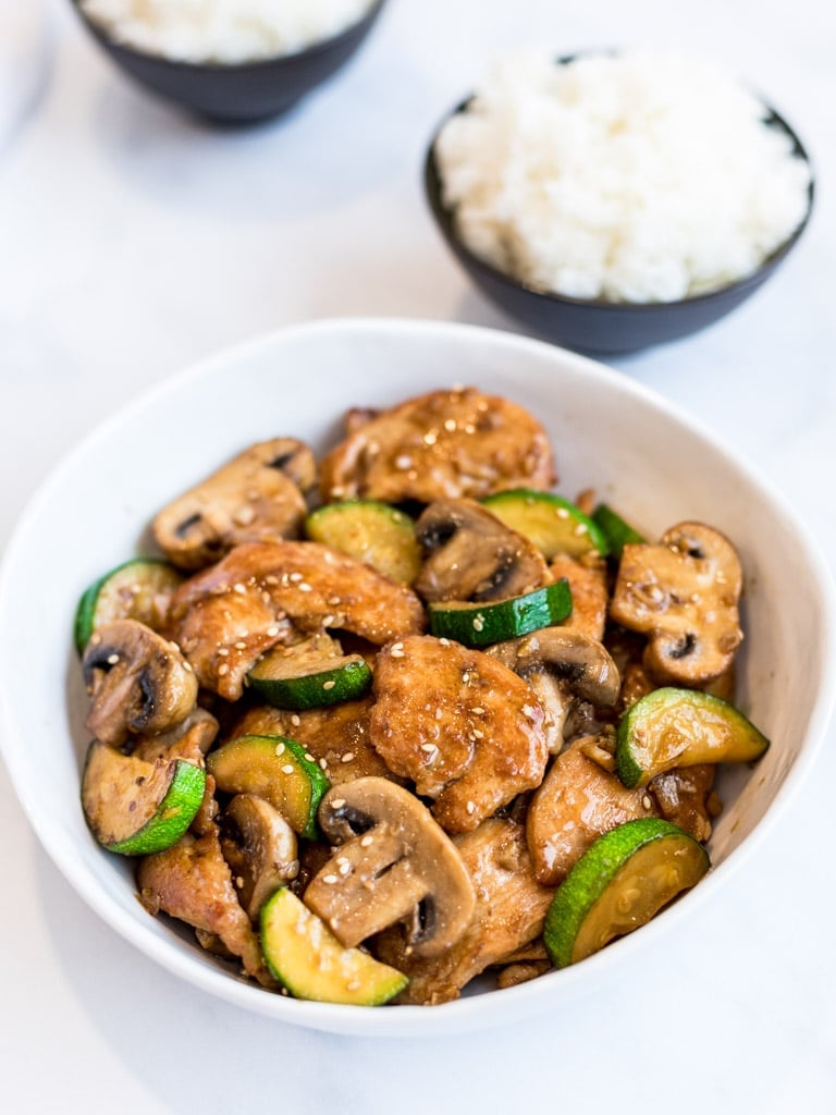 Panda Express mushroom chicken copycat in a white bowl with bowls of rice