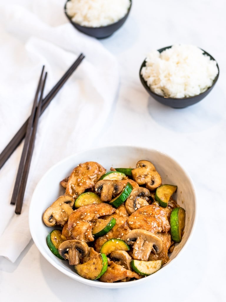Panda Express mushroom chicken copycat in a white bowl with bowls of rice and chopsticks