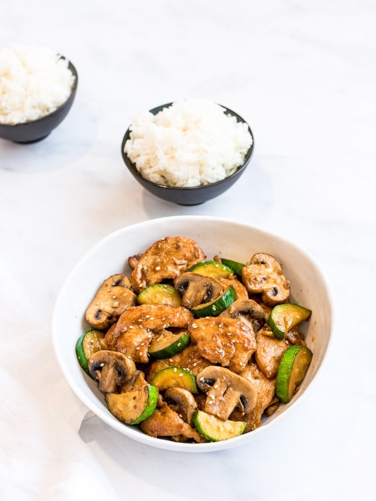 Panda Express mushroom chicken copycat in a white bowl with bowls of rice