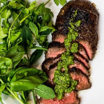 Asian marinated flank steak, spicy Asian chimichurri steak with fresh herbs on a white plate