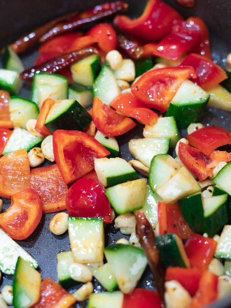 stir fried red peppers, zucchini, chilis, and peanuts in a pan