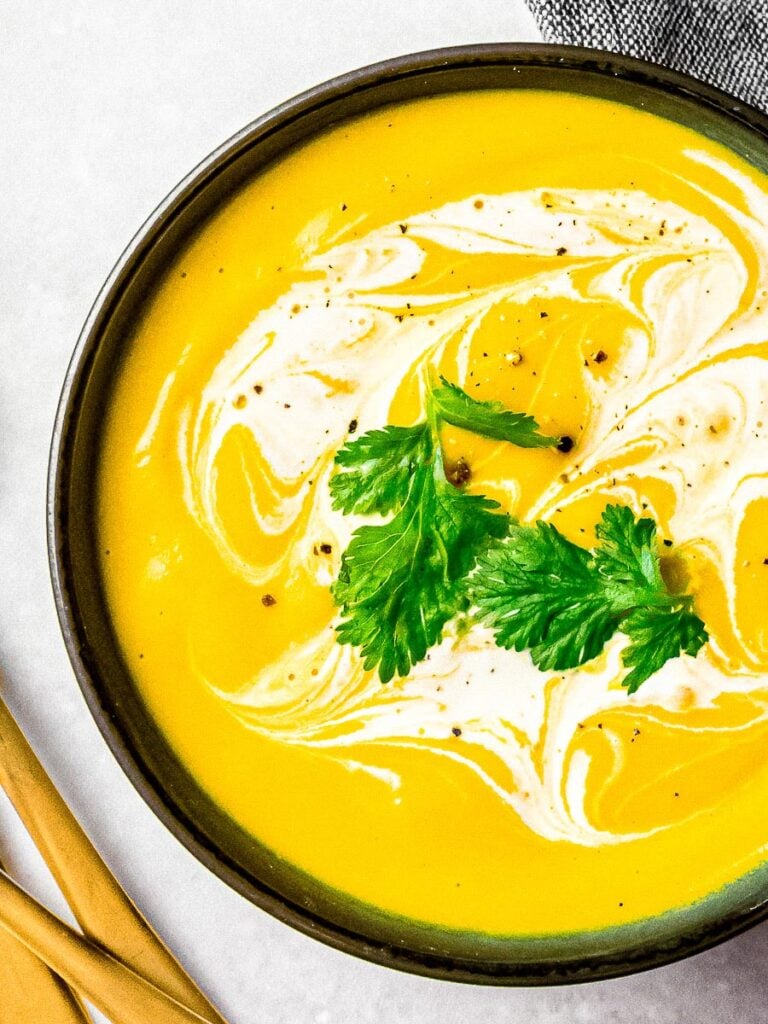 roasted kabocha squash soup, vegan pumpkin soup in a black bowl with cream and herb garnish