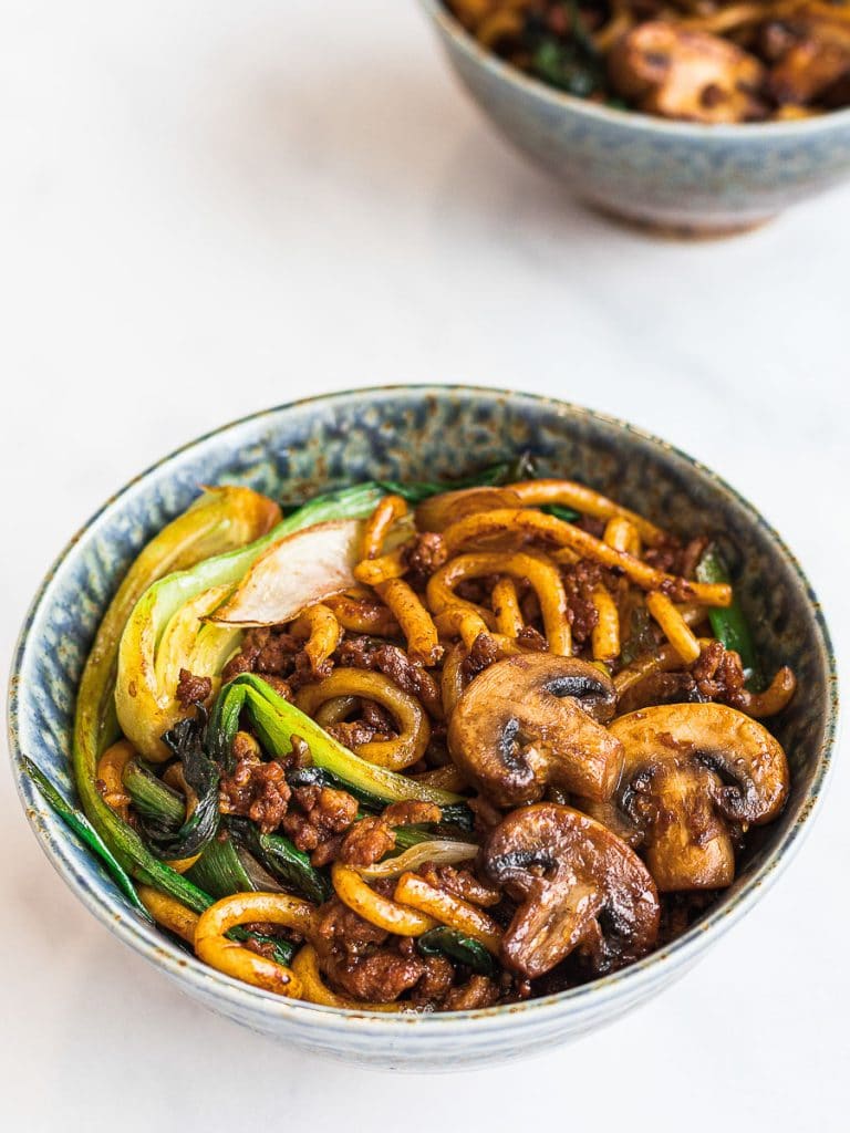 yaki udon, stir fried udon noodles with mushrooms and bok choy in a blue bowl