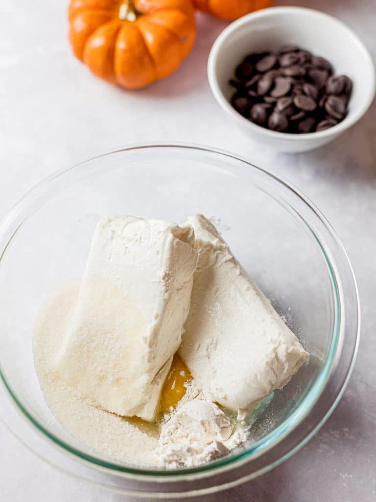 cream cheese filling ingredients in a bowl next to chocolate chips and pumpkins