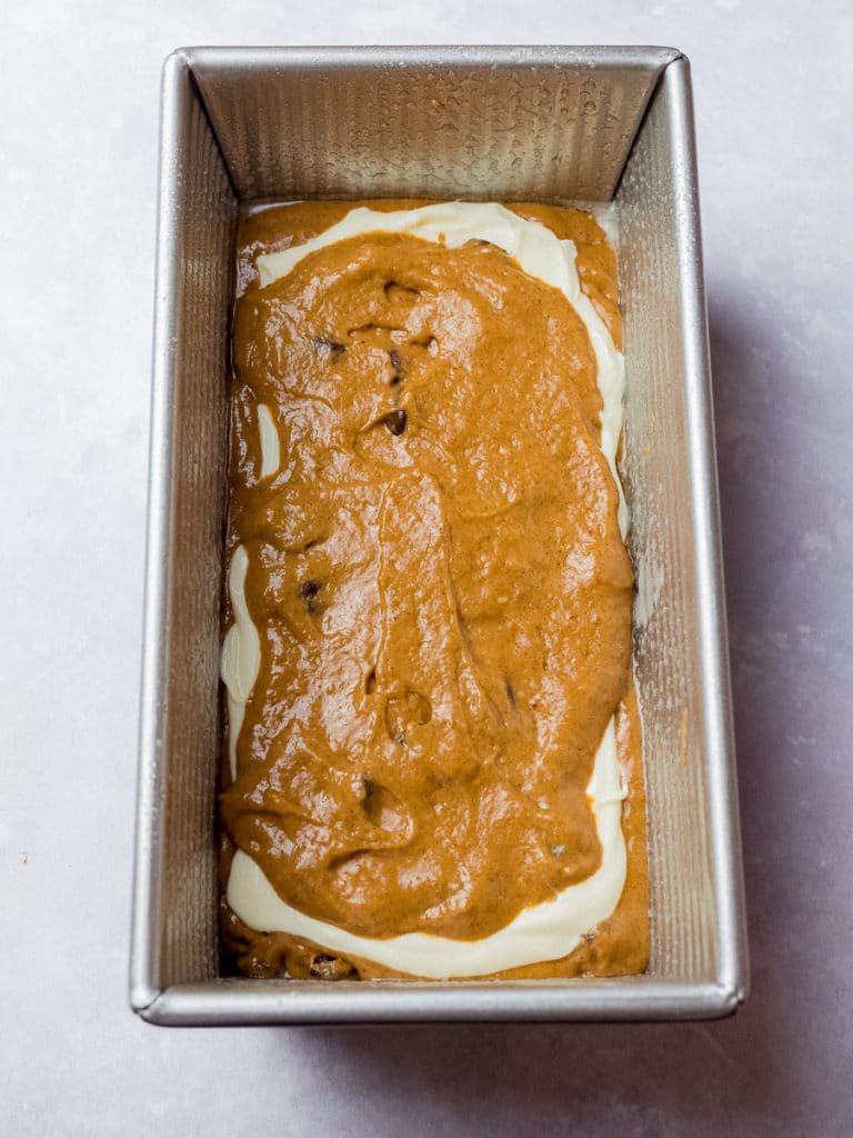 pumpkin chocolate chip bread batter with cream cheese layer in a loaf pan