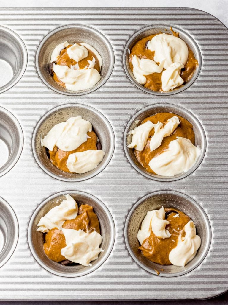 pumpkin chocolate chip muffin batter and cream cheese filling in a muffin tin