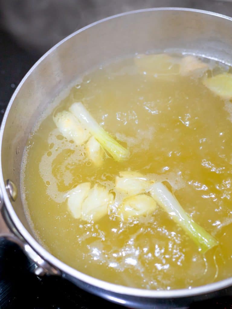 Asian flavored broth in a pot with garlic, scallions, and ginger