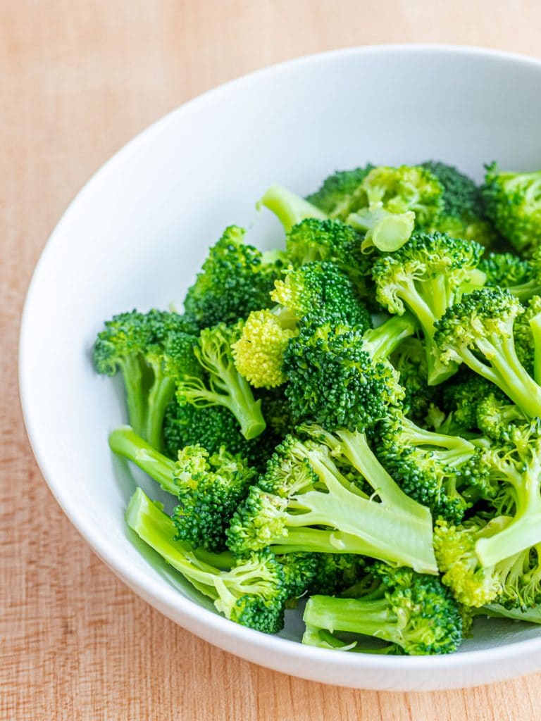 a white bowl with blanched broccoli on a wooden surface