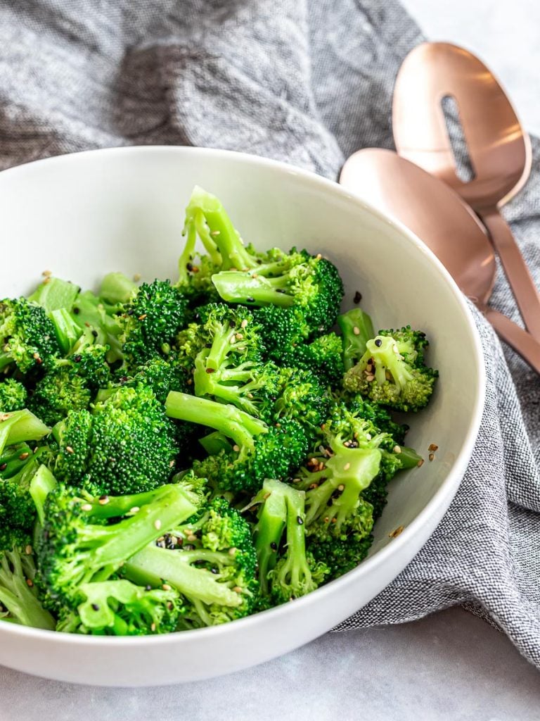 Asian sesame broccoli salad in a white bowl next to serving spoons