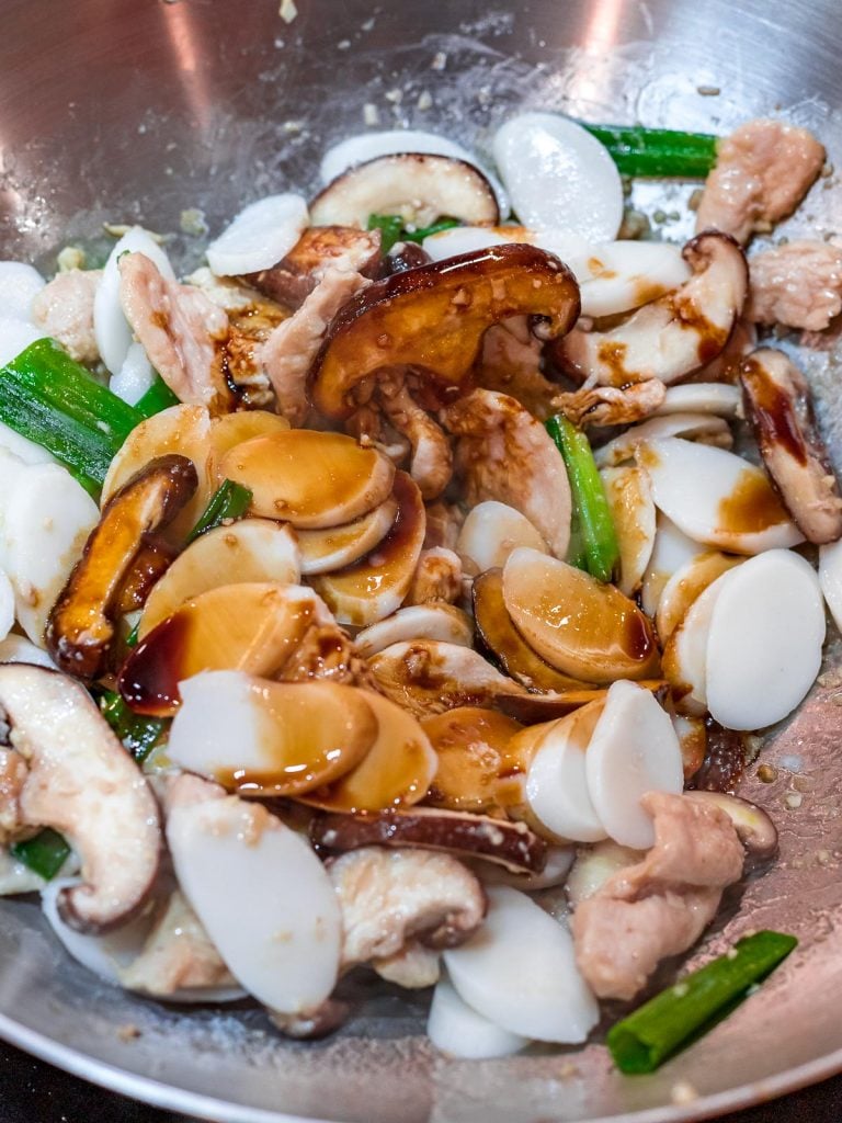 stir fried rice cakes with mushrooms, chicken, and scallions in a wok