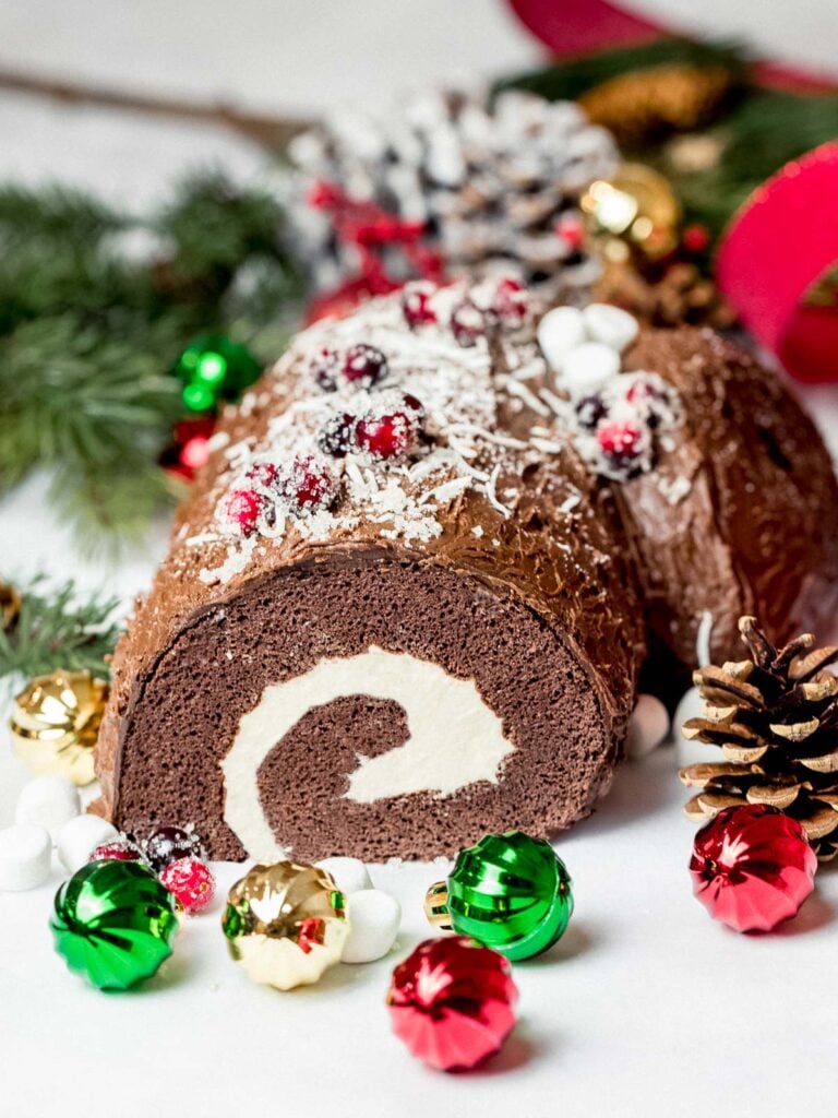 yule log cake or buche de noel decorated with chocolate and marshmallows next to ornaments and pine cones