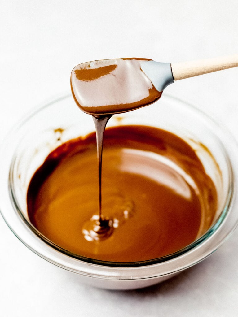 chocolate ganache dripping off a spatula into a glass bowl