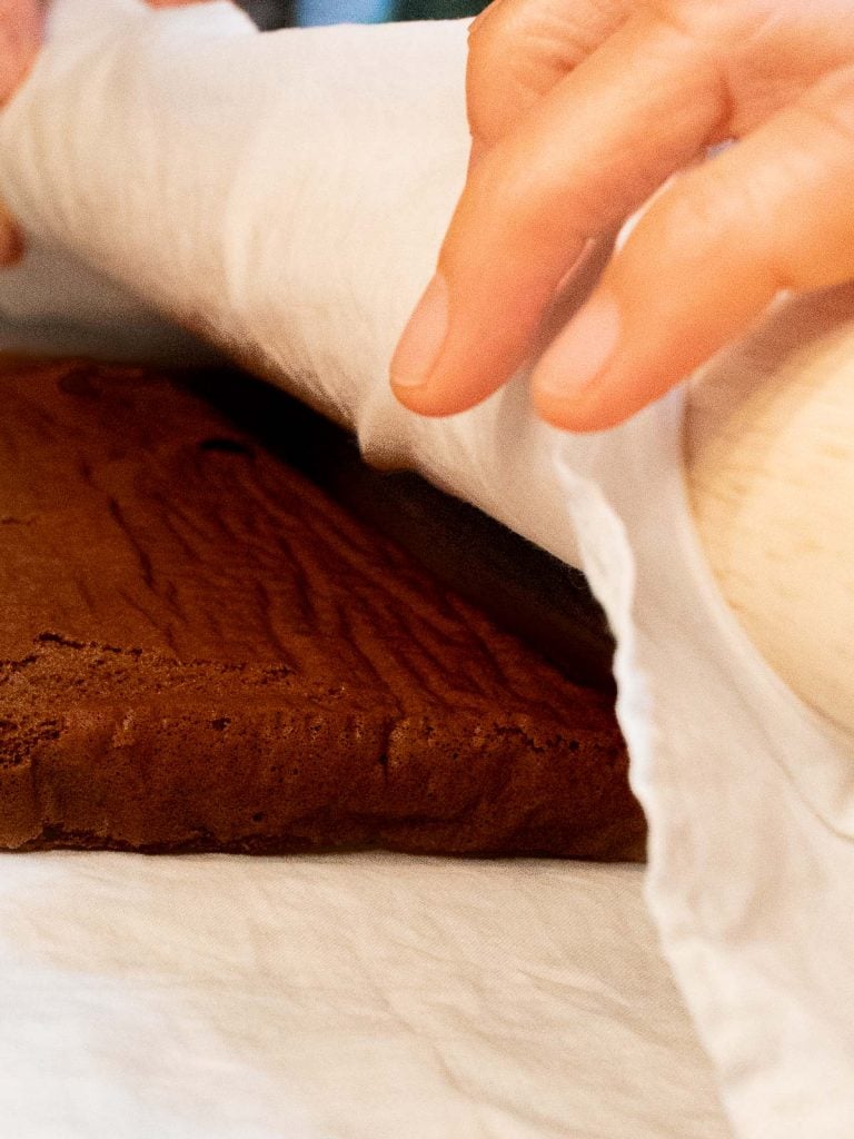 rolling up chocolate swiss roll cake in a kitchen towel