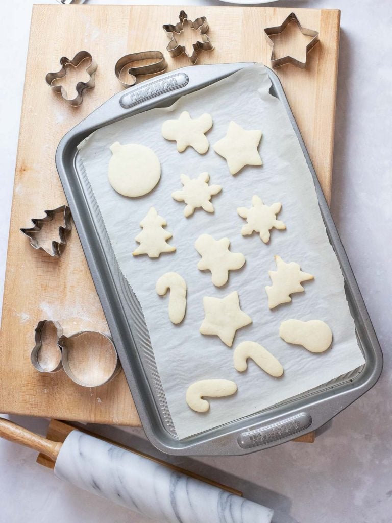soft Christmas sugar cookies on a baking tray next to cookie cutters