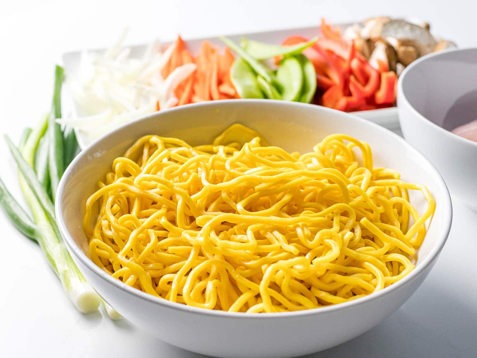 fresh Chinese egg noodles next to vegetables in a white bowl
