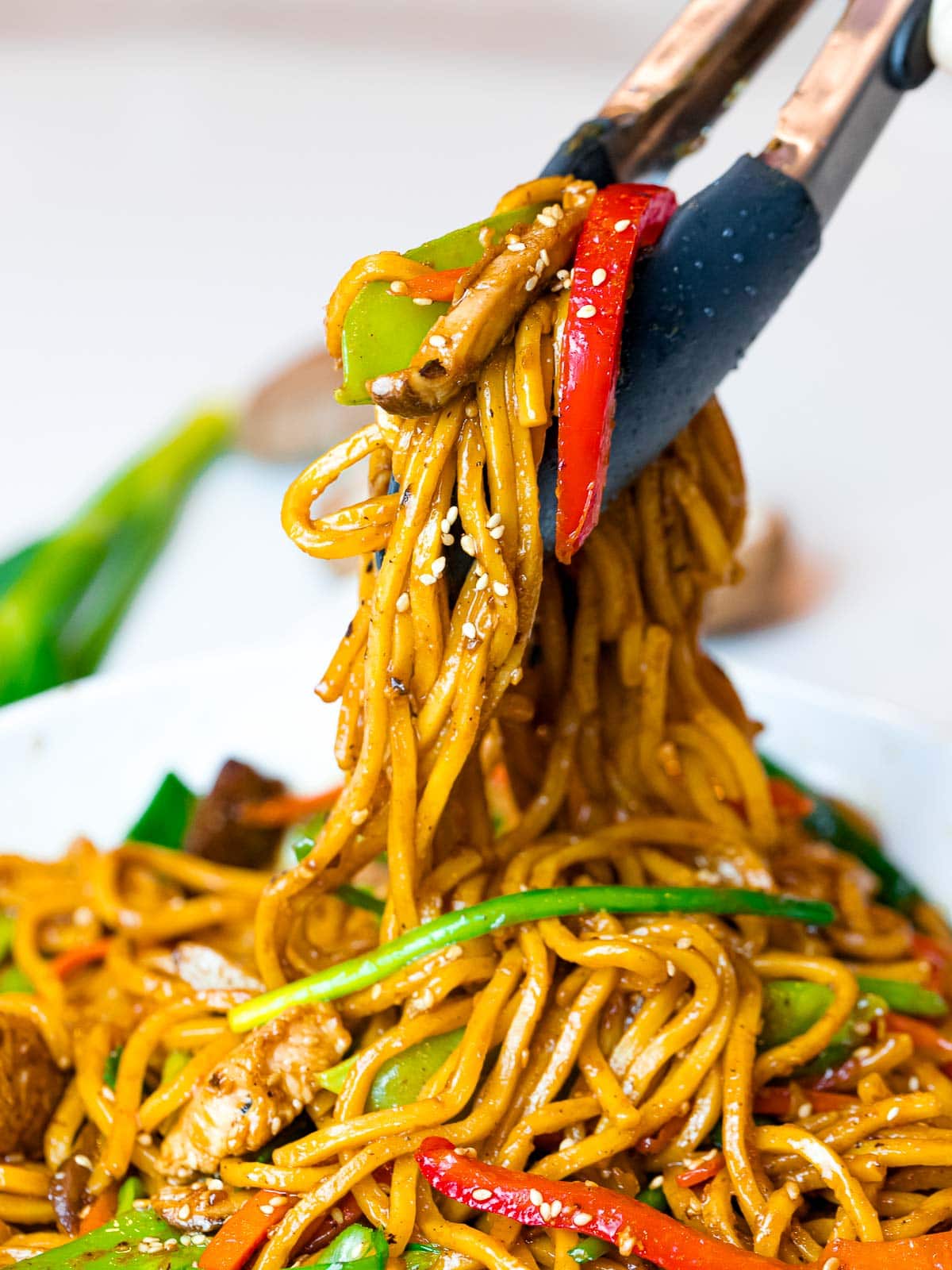 easy chicken lo mein with vegetables held by tongs